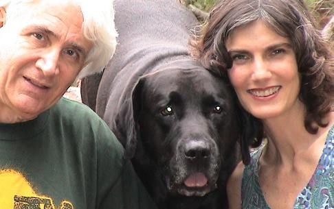 A man and a woman are posing for a picture with a black dog