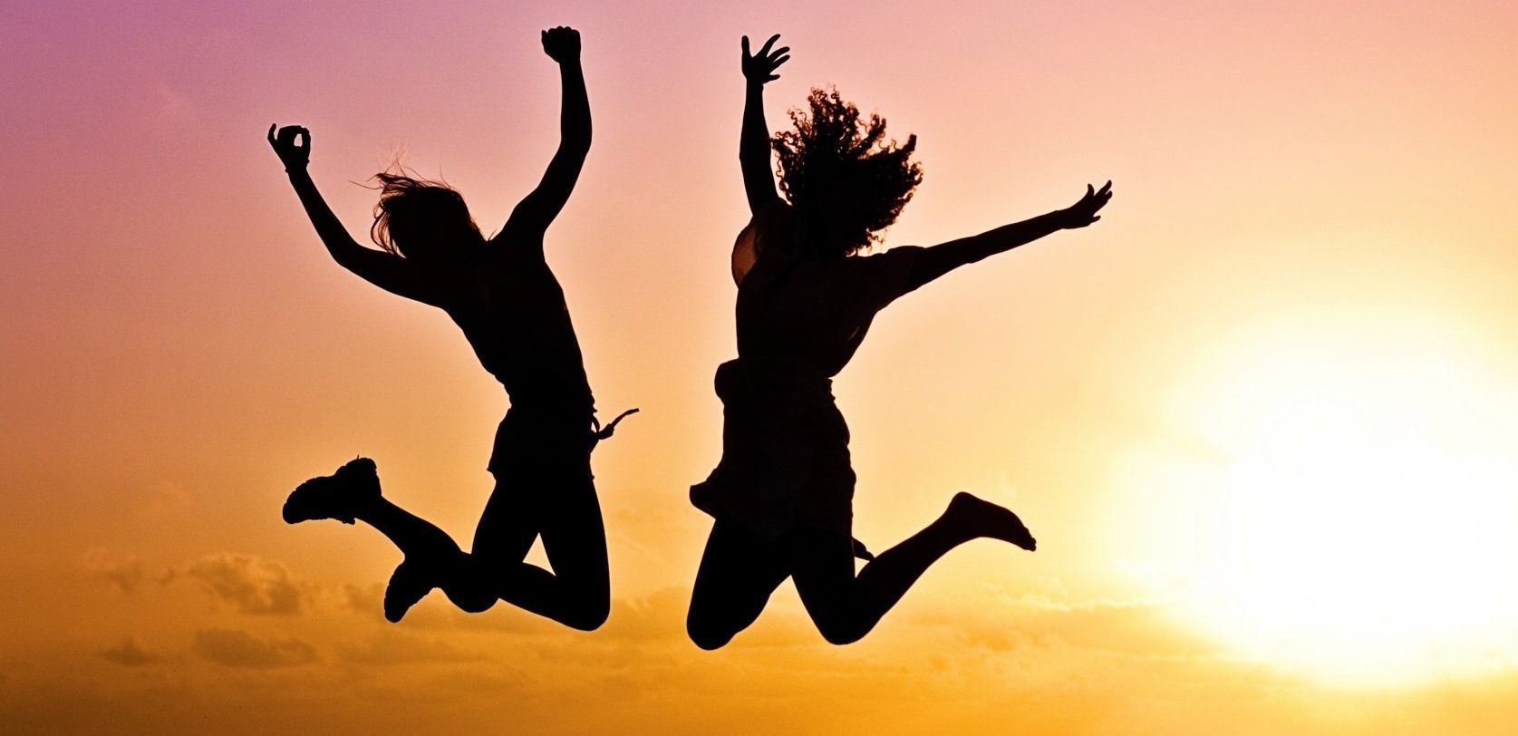 Two people are jumping in the air at sunset.