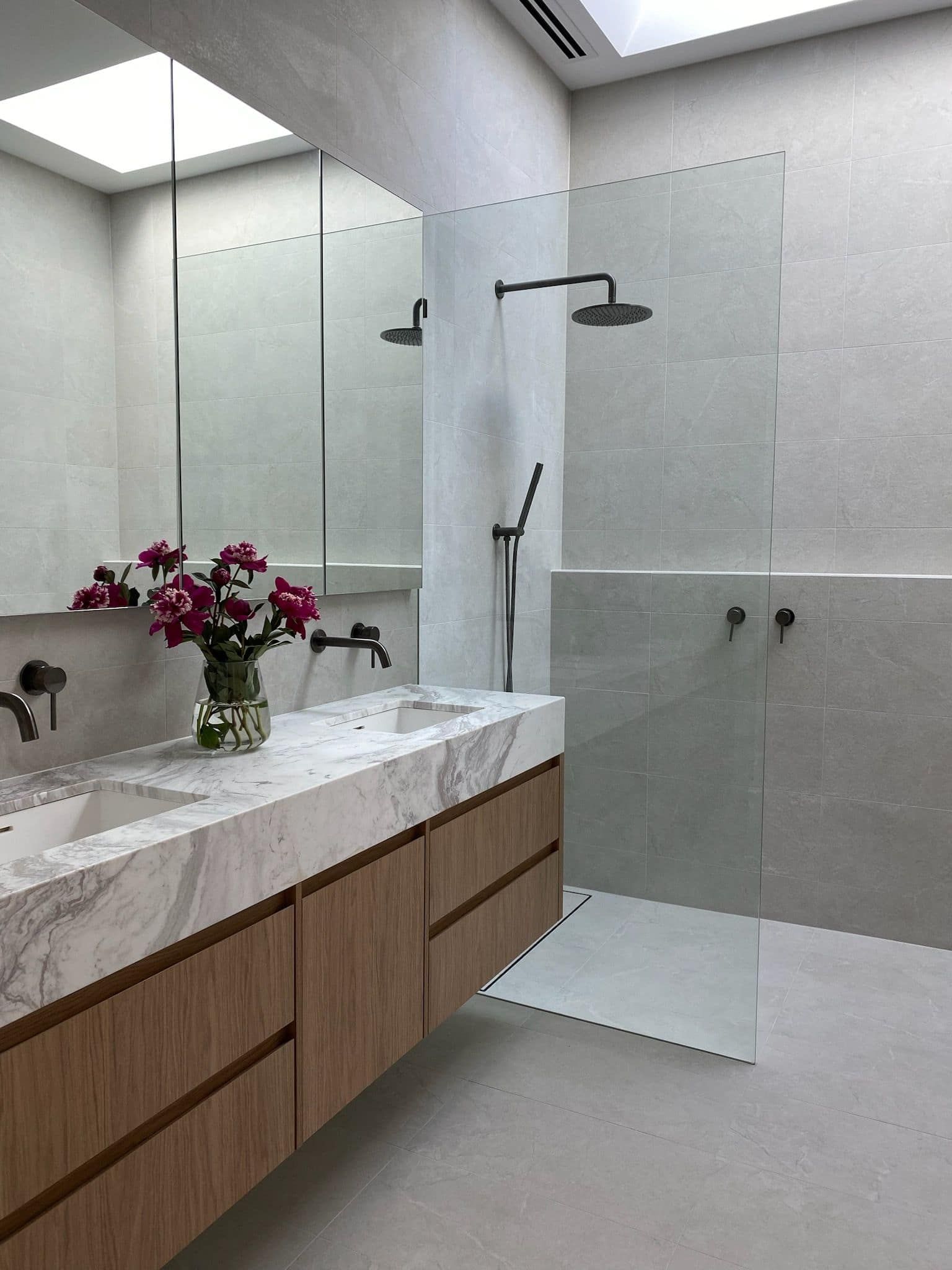 A bathroom with two sinks , a shower and a mirror.