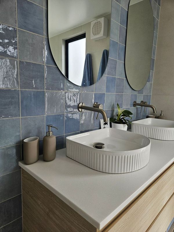 A bathroom with two sinks , two mirrors and blue tiles.