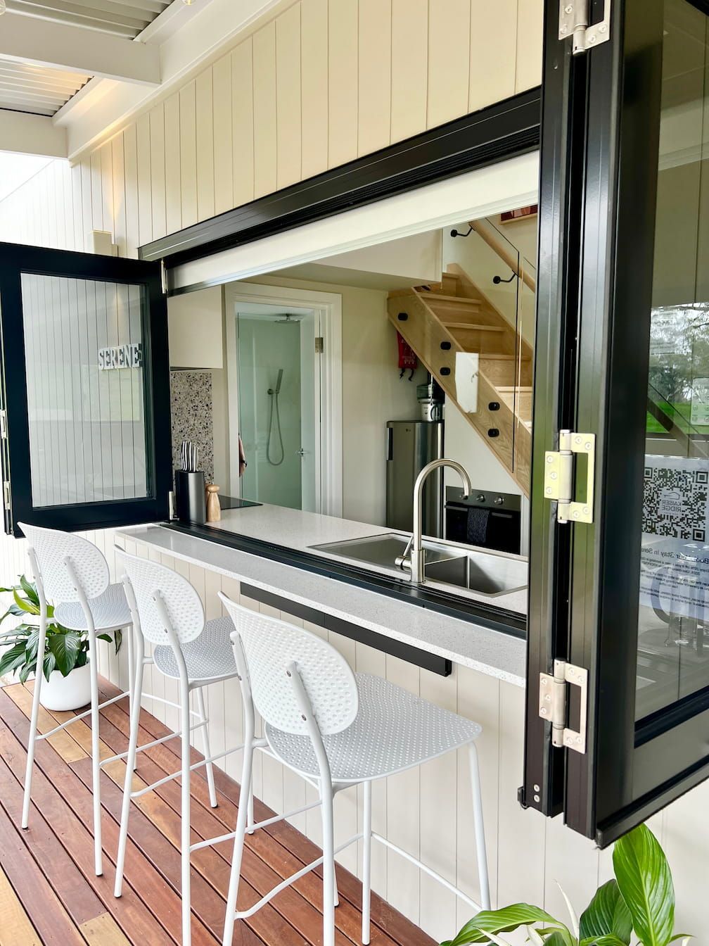 A kitchen with a sink , stools and a large window.