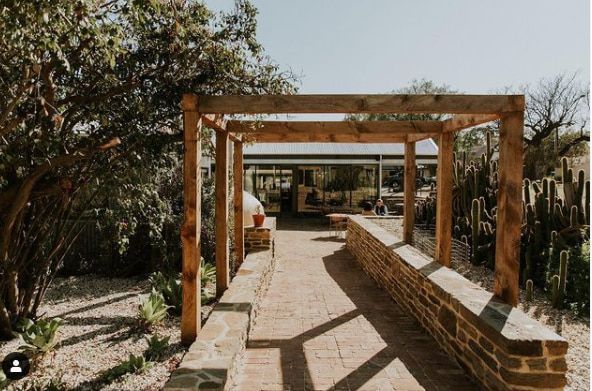 A wooden pergola over a brick walkway leading to a house.