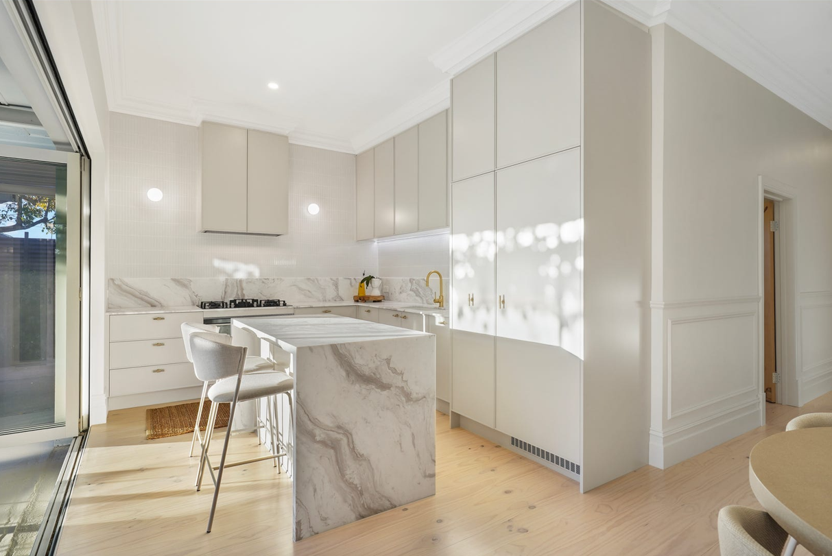 A kitchen with white cabinets , marble counter tops , and a large island.