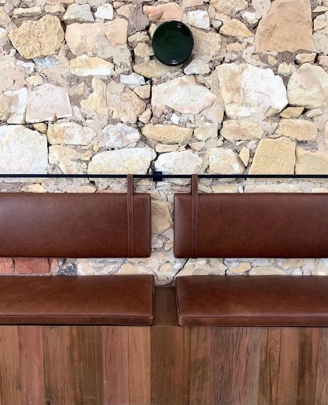 Two brown leather benches are sitting in front of a stone wall.