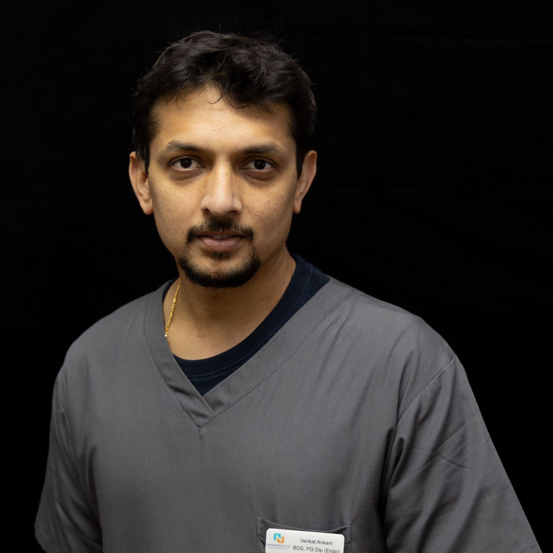 A man with a beard wearing a grey scrub top