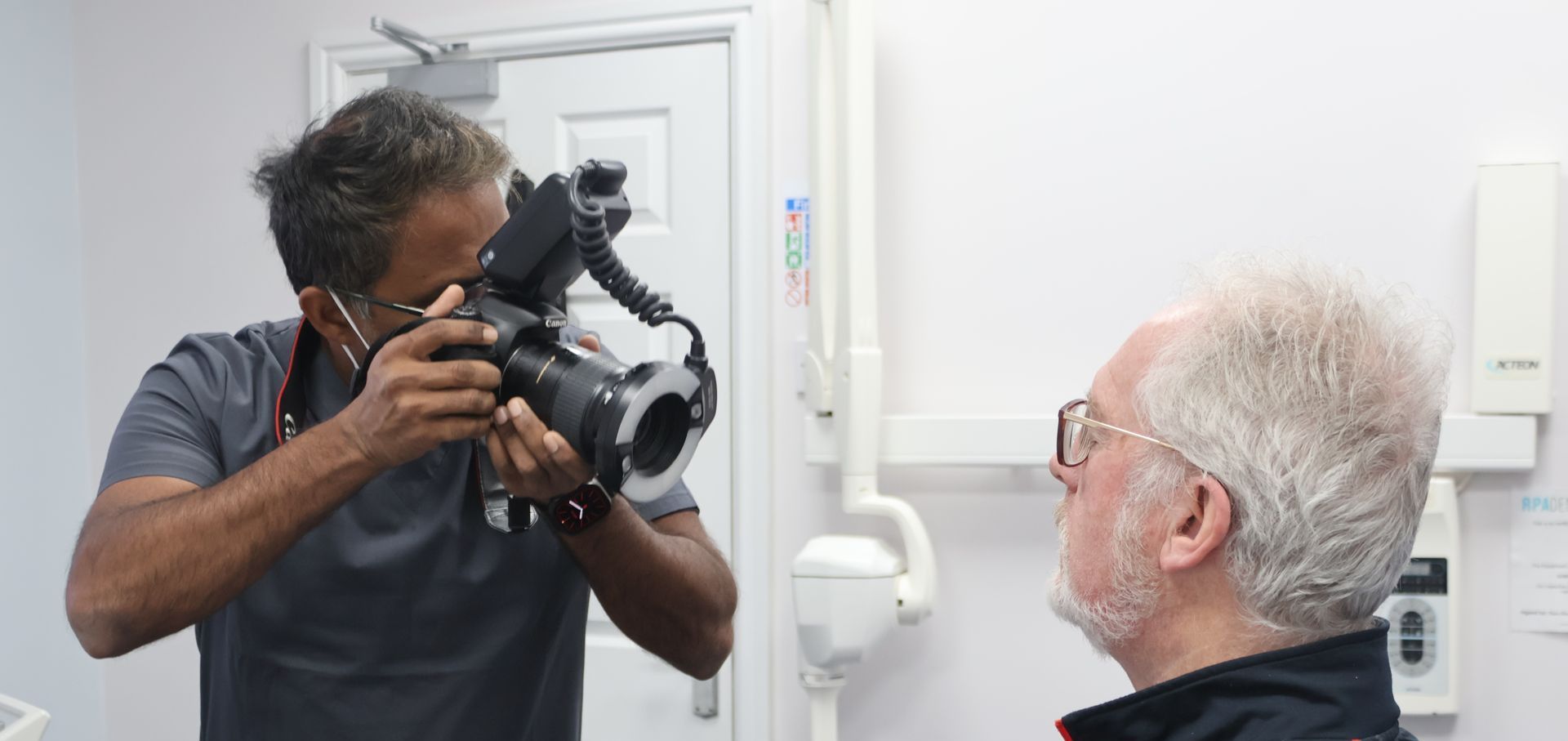 a man is taking a clinical before photo of a patient smiling for his dental records. canon camera is being used.