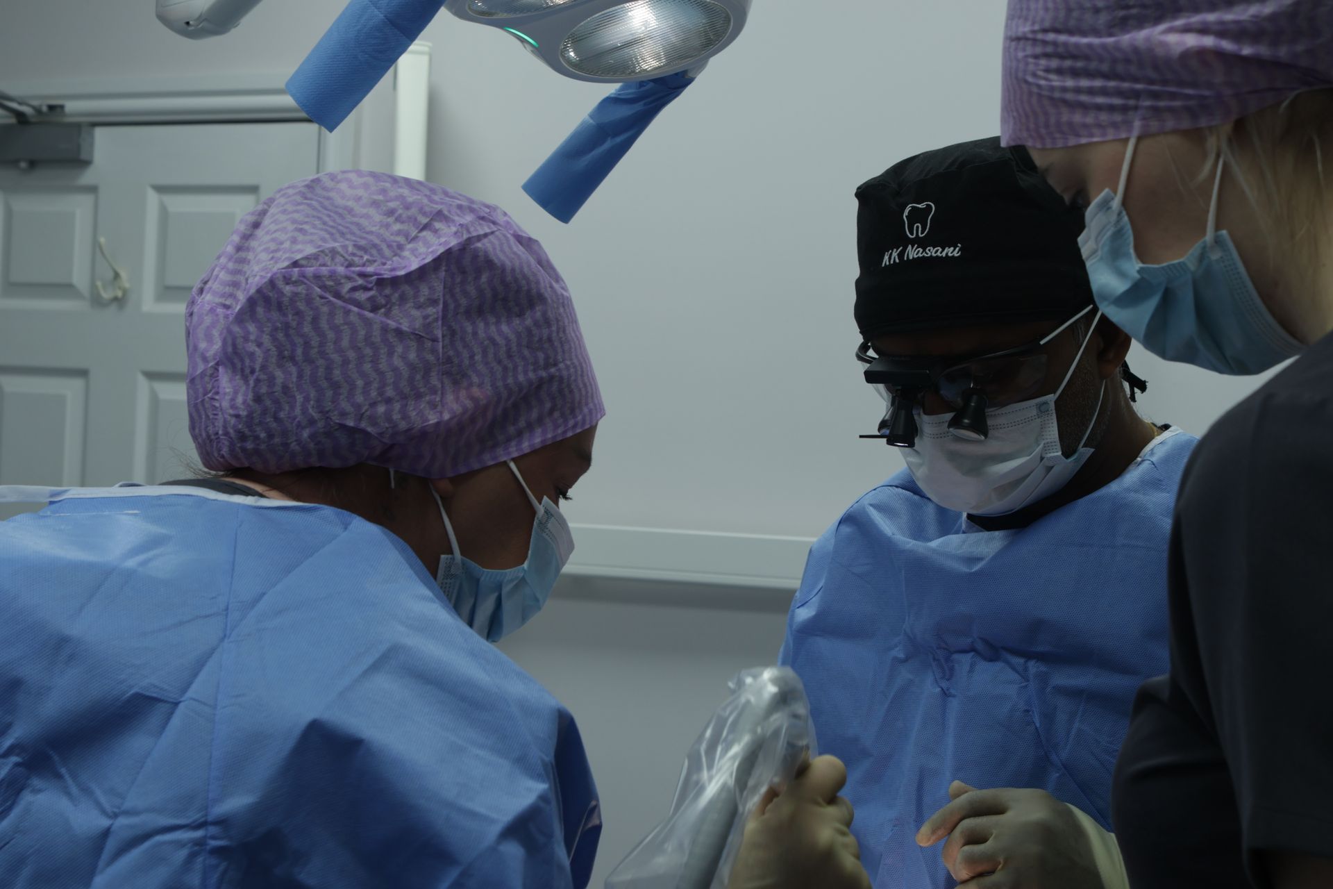 Medical team in an operating room; surgeons in scrubs and masks attending a patient for dental implants.
