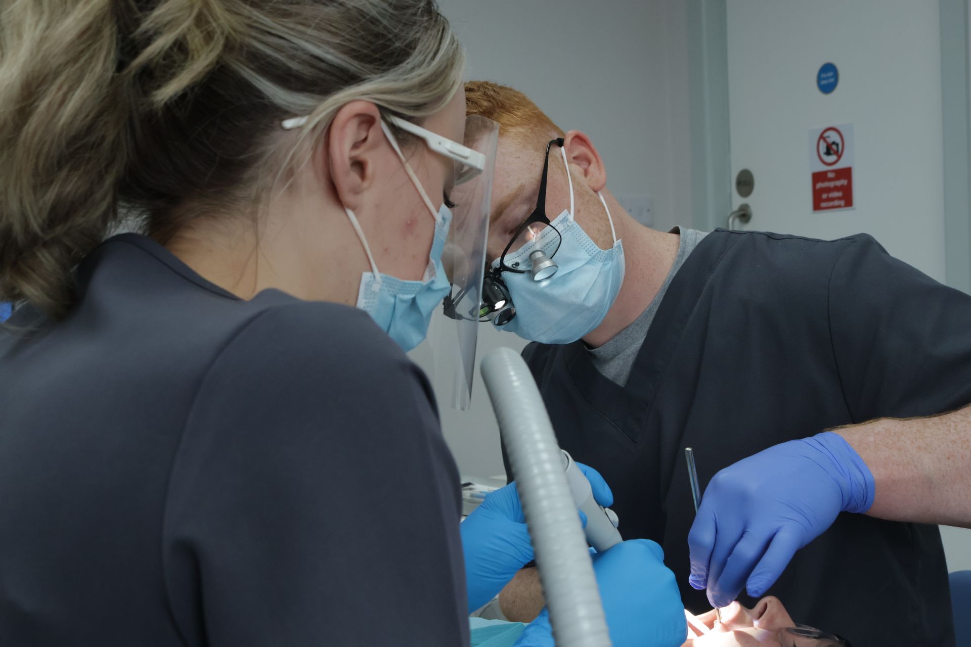 Two female dentists are working on a patient 's teeth.. performing a scale and polish 