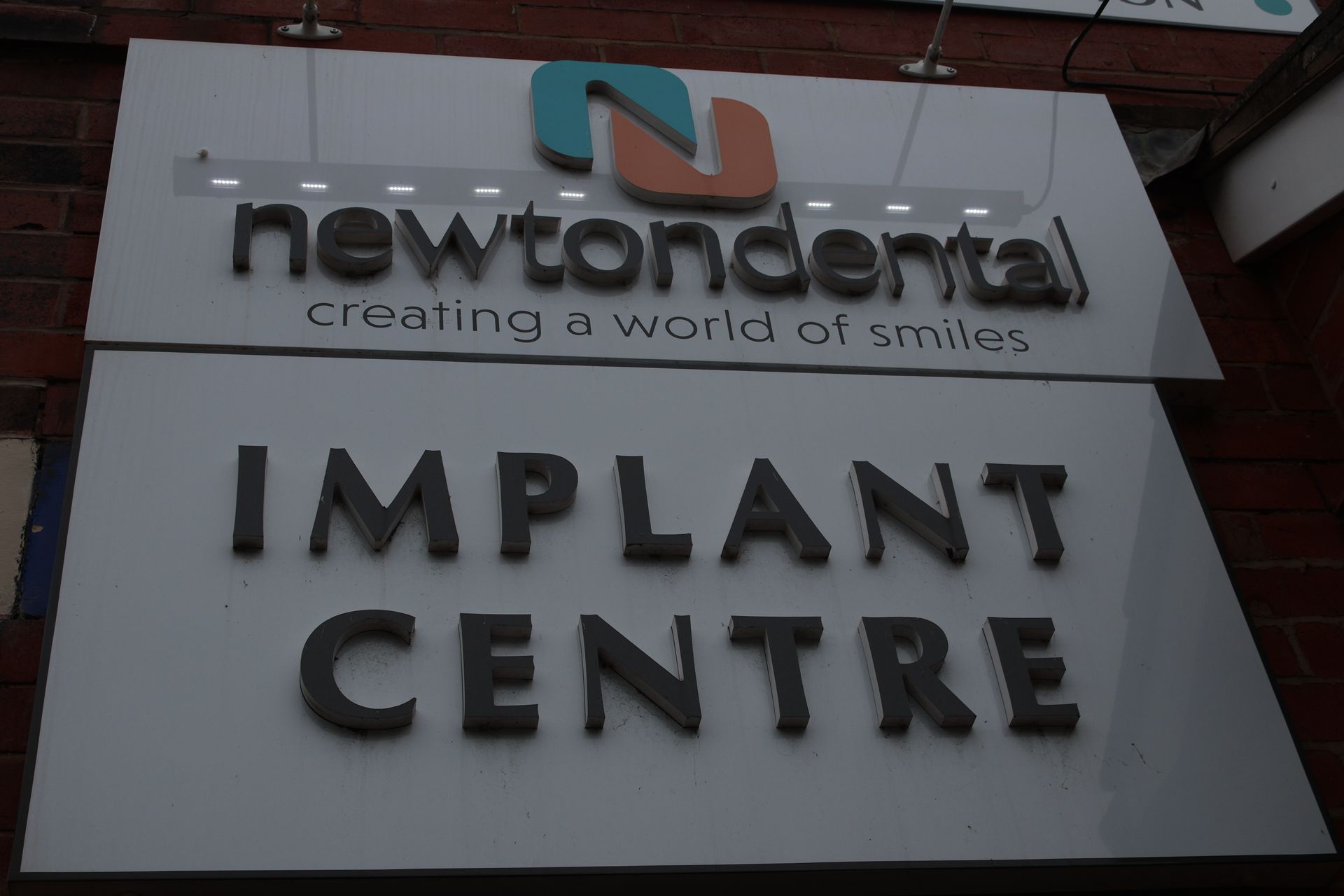 Sign for Newton Dental Implant Centre with logo, text and dark lettering.