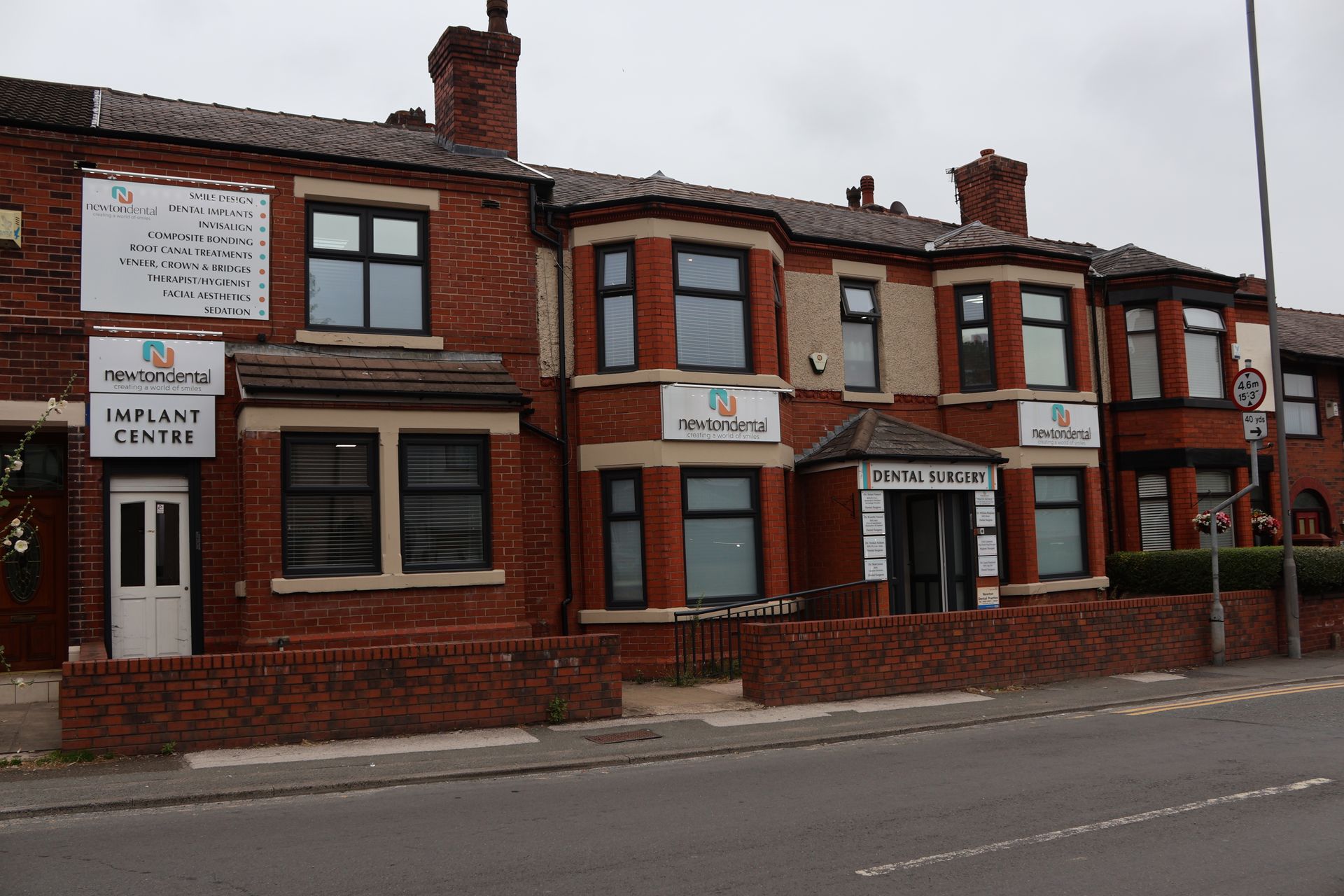Red brick row of buildings, each with office signage of a dental practice, newton dental. Street view.