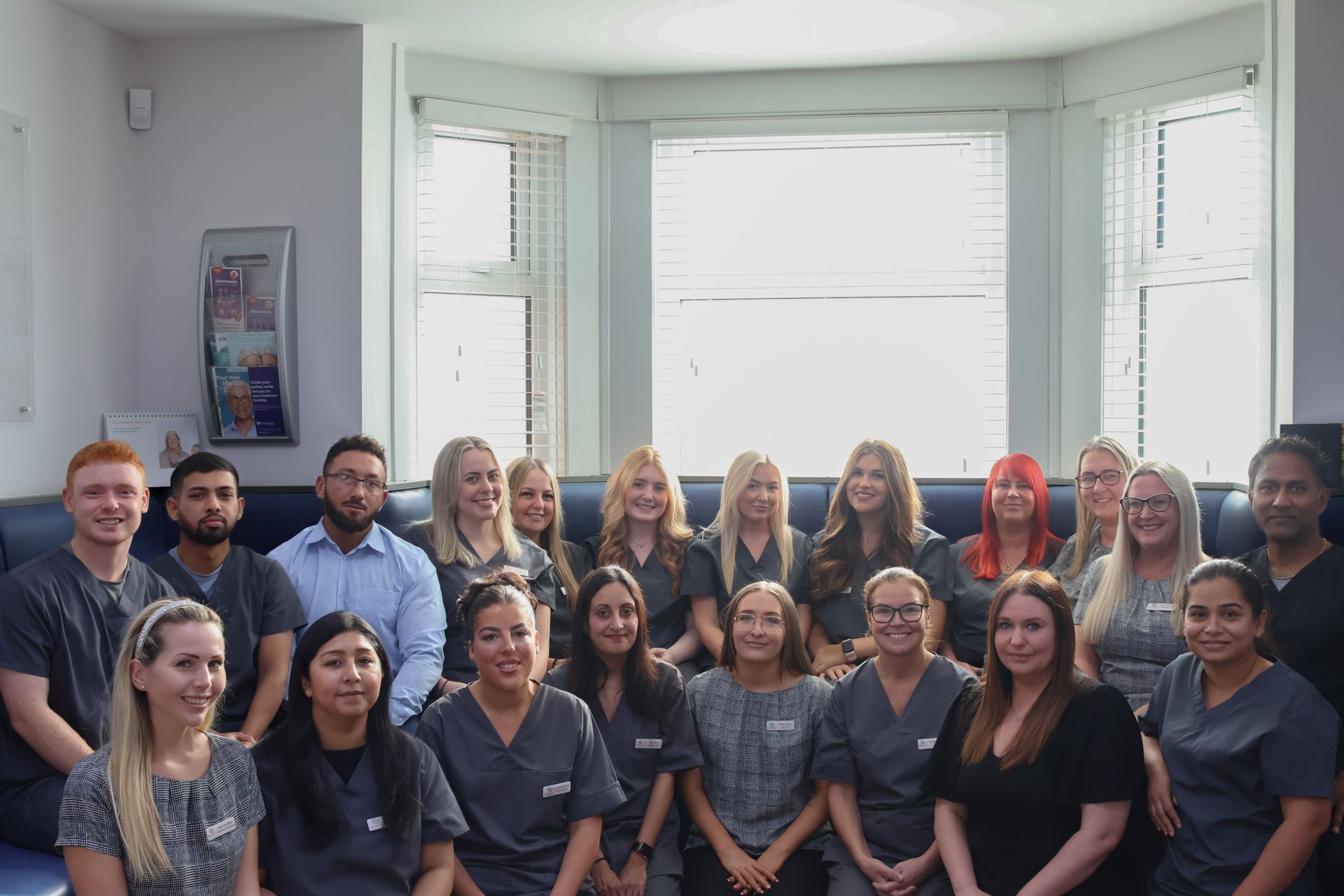 Group of dental clinic staff smiling, posing inside near a window.