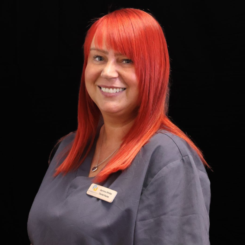 A woman with long red  hair is wearing a scrub and smiling.
