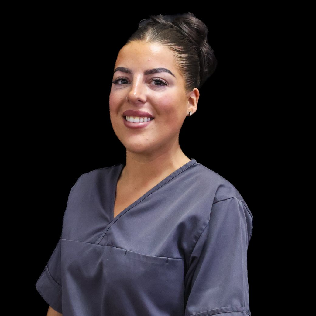 A woman with hair in a styled bun  is wearing a grey scrub and smiling for the camera.