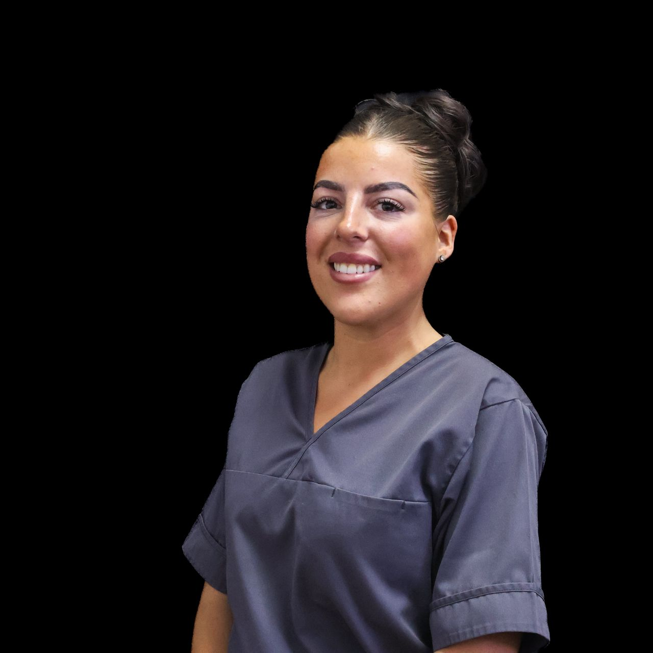 A woman with hair in a styled bun is wearing a grey scrub and smiling for the camera.