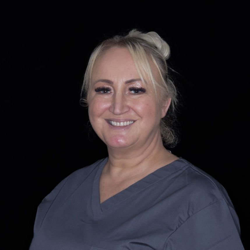 A woman in a blue scrub top is smiling in front of a black background.