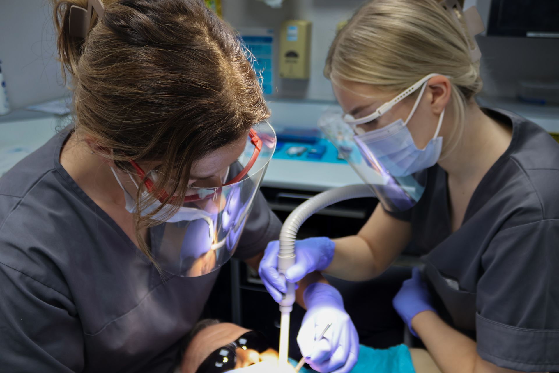 Two female dentists are working on a patient 's teeth.. performing a scale and polish 