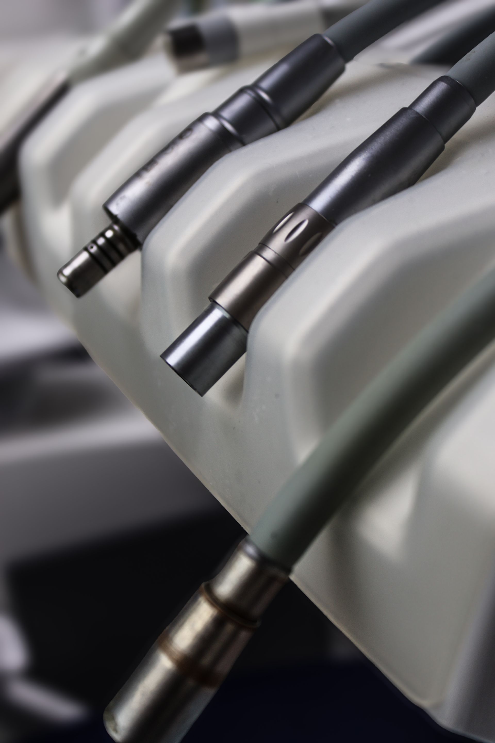 Close-up view of several handpieces with silver metal tips and grey tubing, ready for use in a dental surgery. 