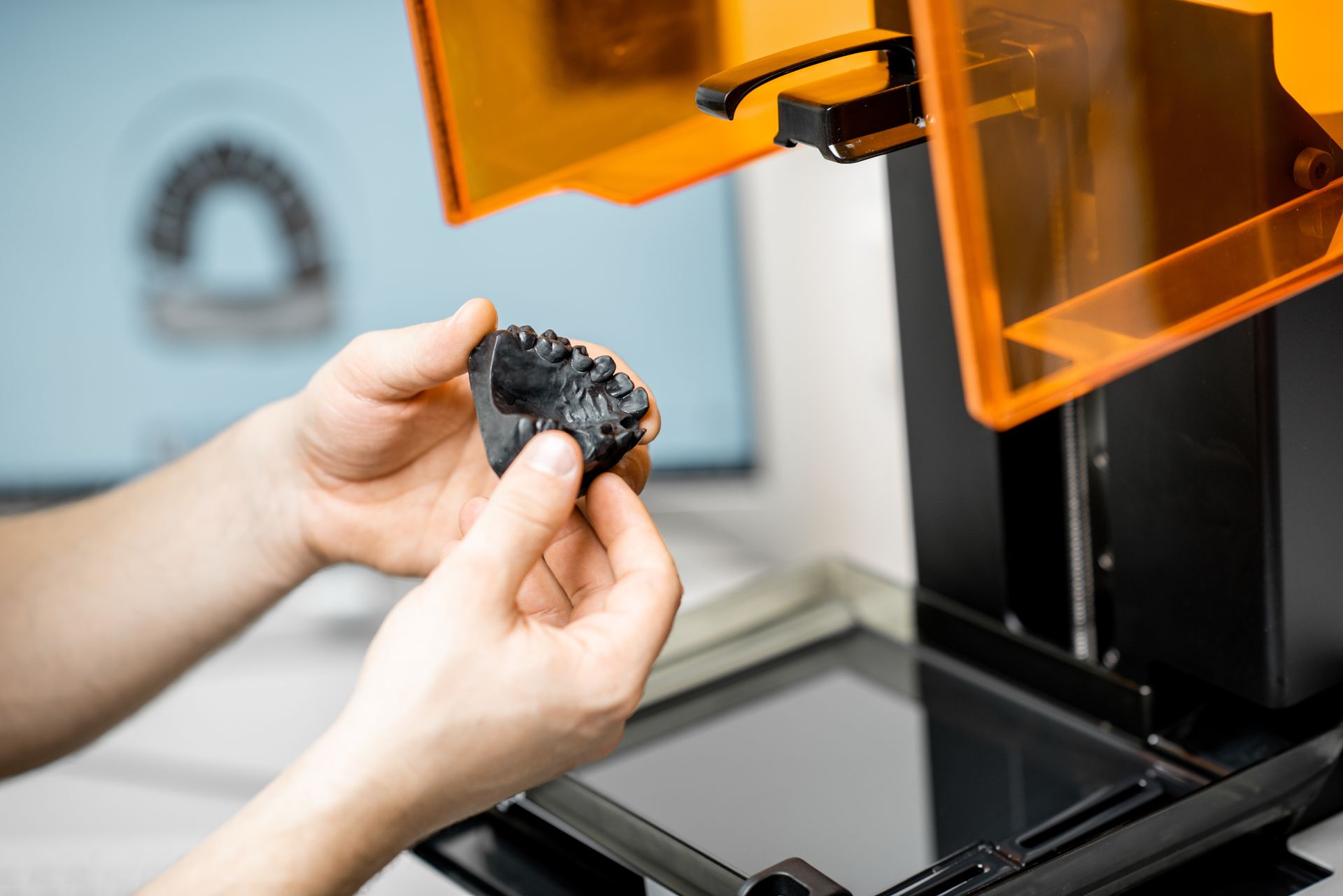 A person is holding a piece of wood in front of a 3d printer.