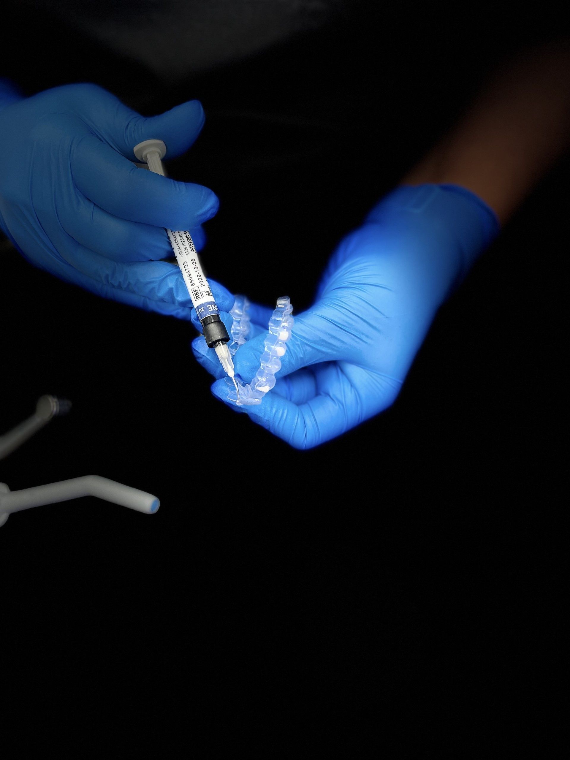 A person wearing blue gloves is holding a syringe and a clear