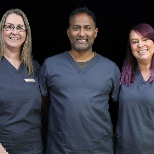 A man and two women are posing for a picture together. Dental professionals 