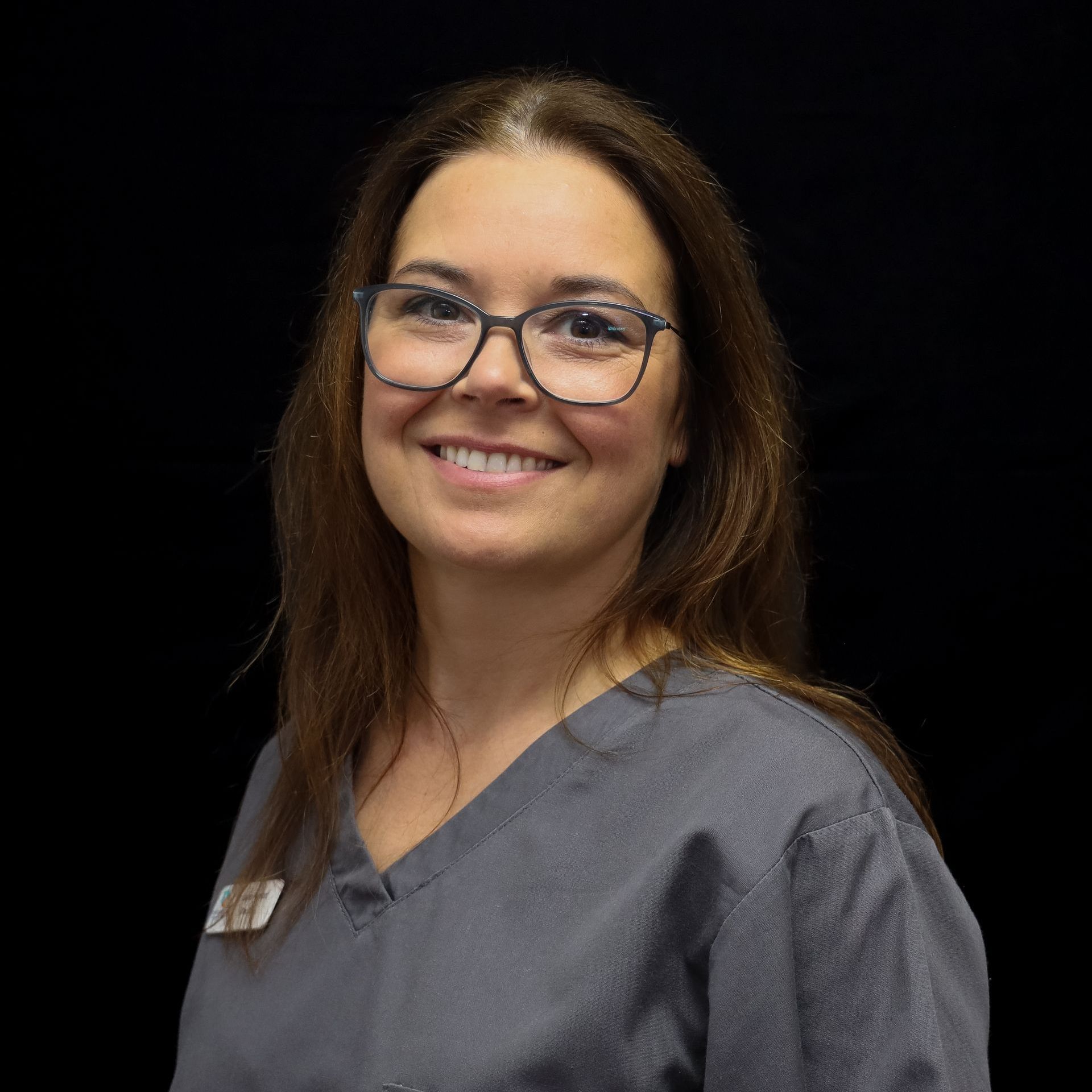 A woman wearing glasses and a scrub top is smiling for the camera.