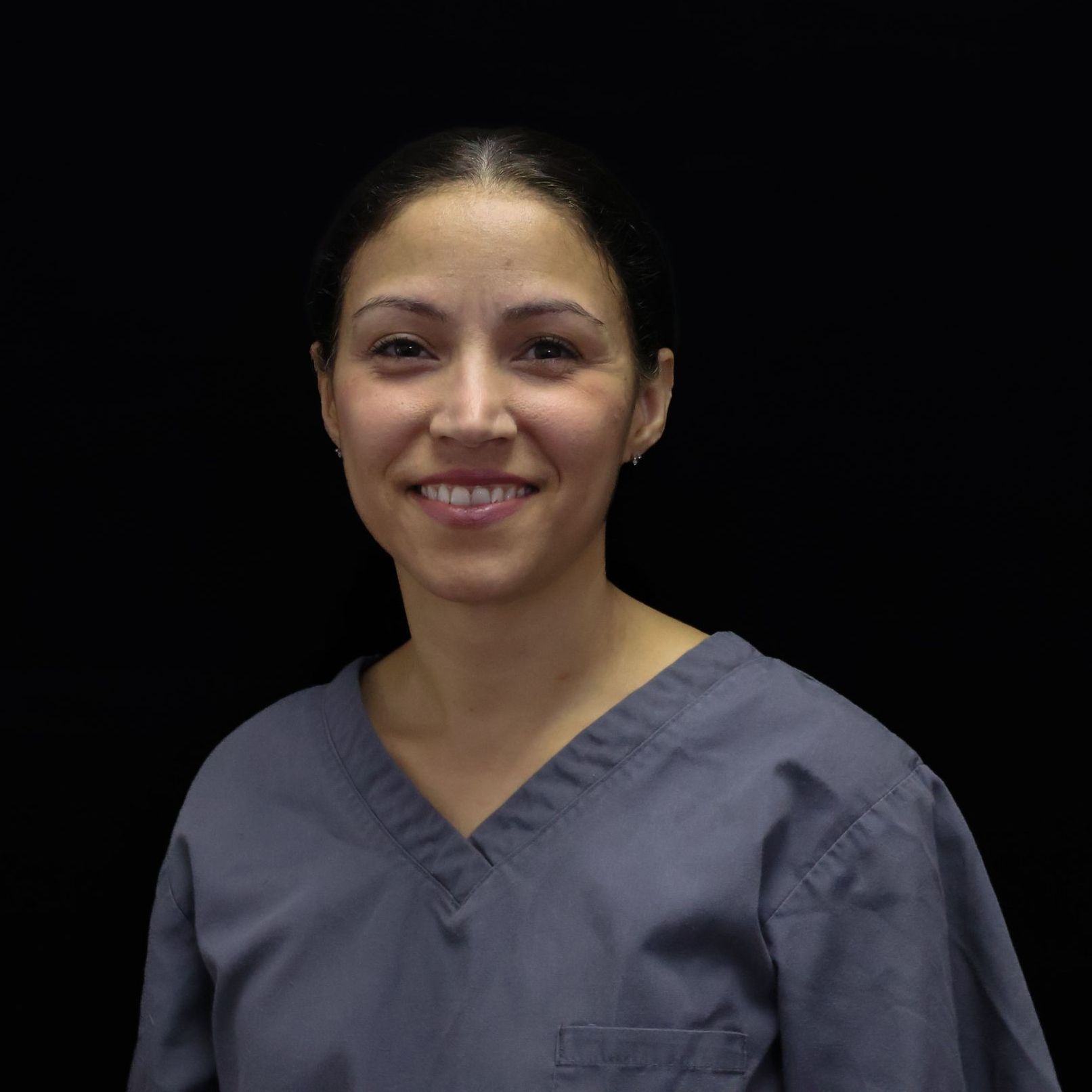 A woman in a grey scrub top smiles for the camera