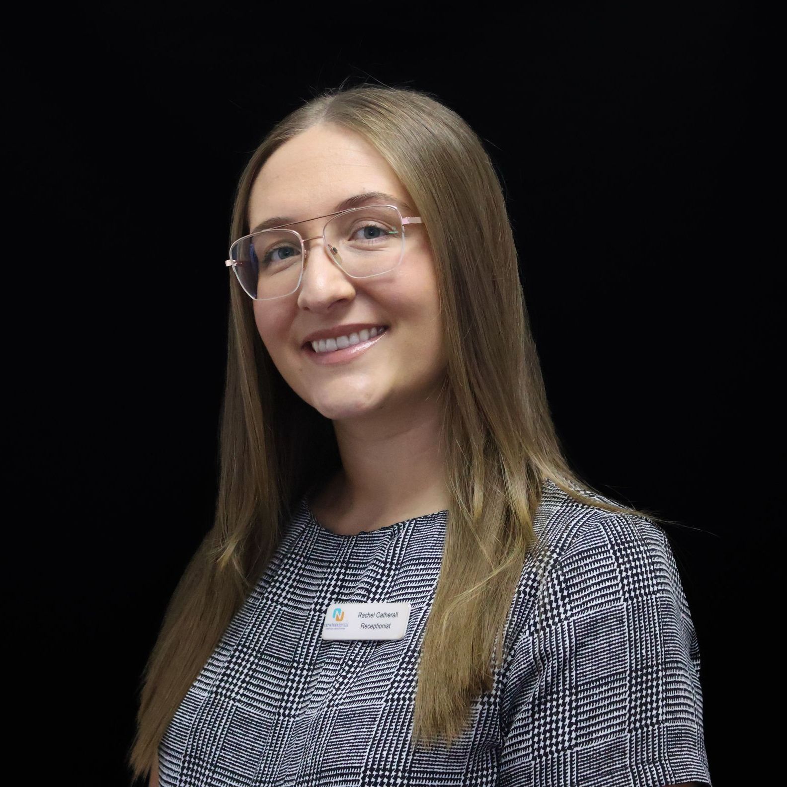 A woman wearing glasses and a name tag is smiling for the camera.