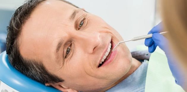 A man is laying in a dental chair while a dentist examines his teeth.