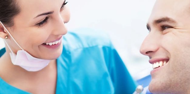 A dentist and a patient are smiling at each other in a dental surgery.