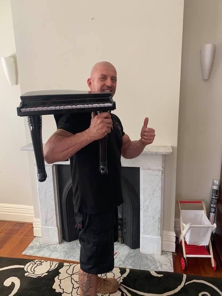A Man Is Holding a Small Piano and Giving a Thumbs Up — Bondi Removals and Taxi Trucks in Randwick, NSW