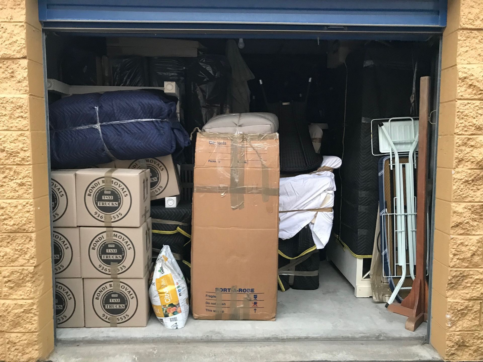 A Man and A Woman Are Carrying Boxes in A Storage Unit — Bondi Removals and Taxi Trucks in Randwick, NSW