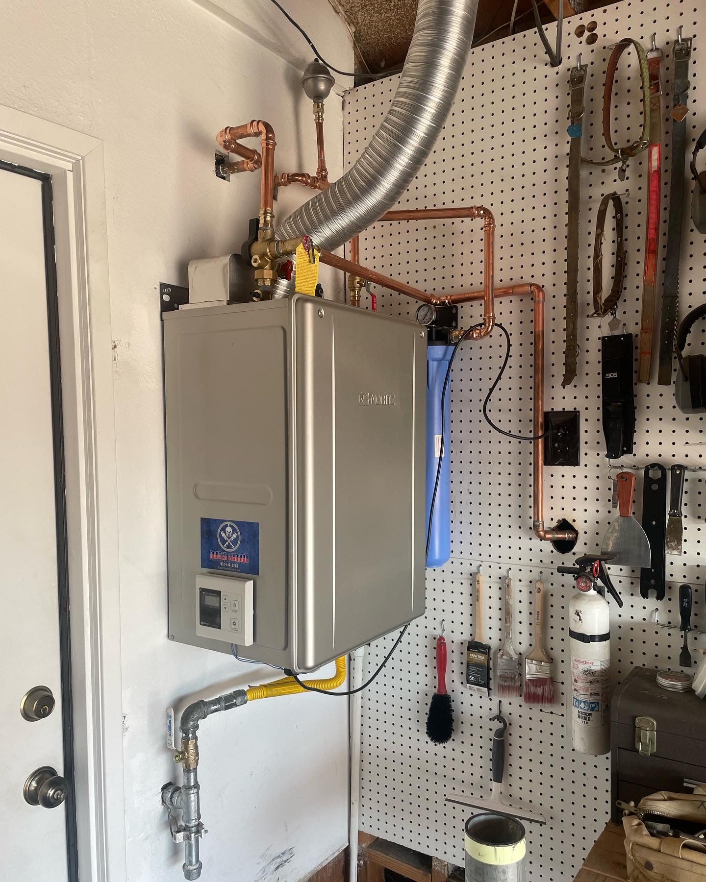 Row of large white industrial water heaters with copper pipes in a utility room