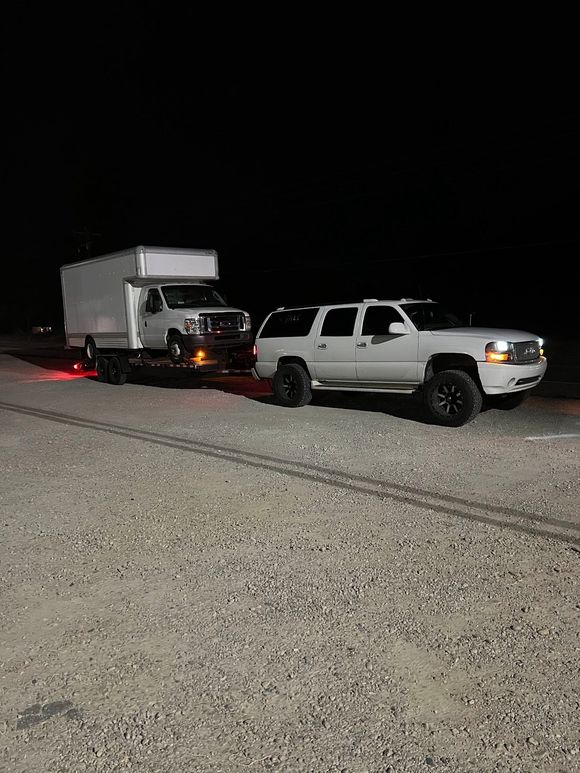 A white truck is towing a trailer down a gravel road at night.