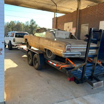 A car is being towed on a trailer in a parking lot