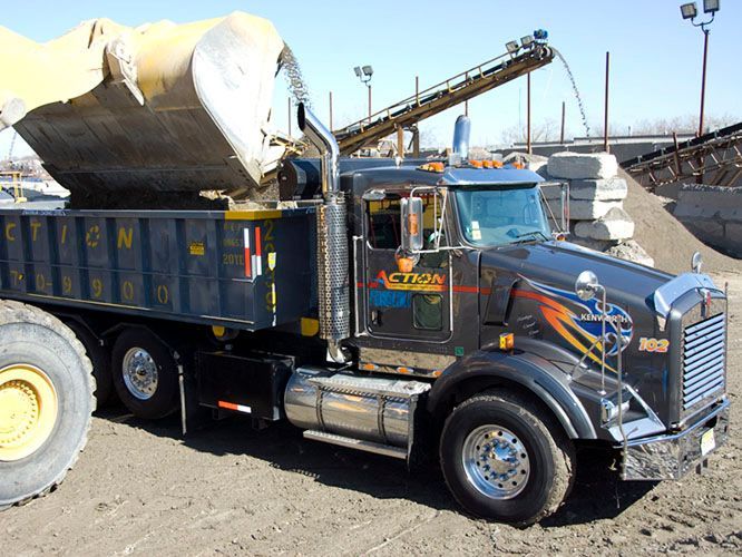 A dump truck is dumping dirt on a dirt road