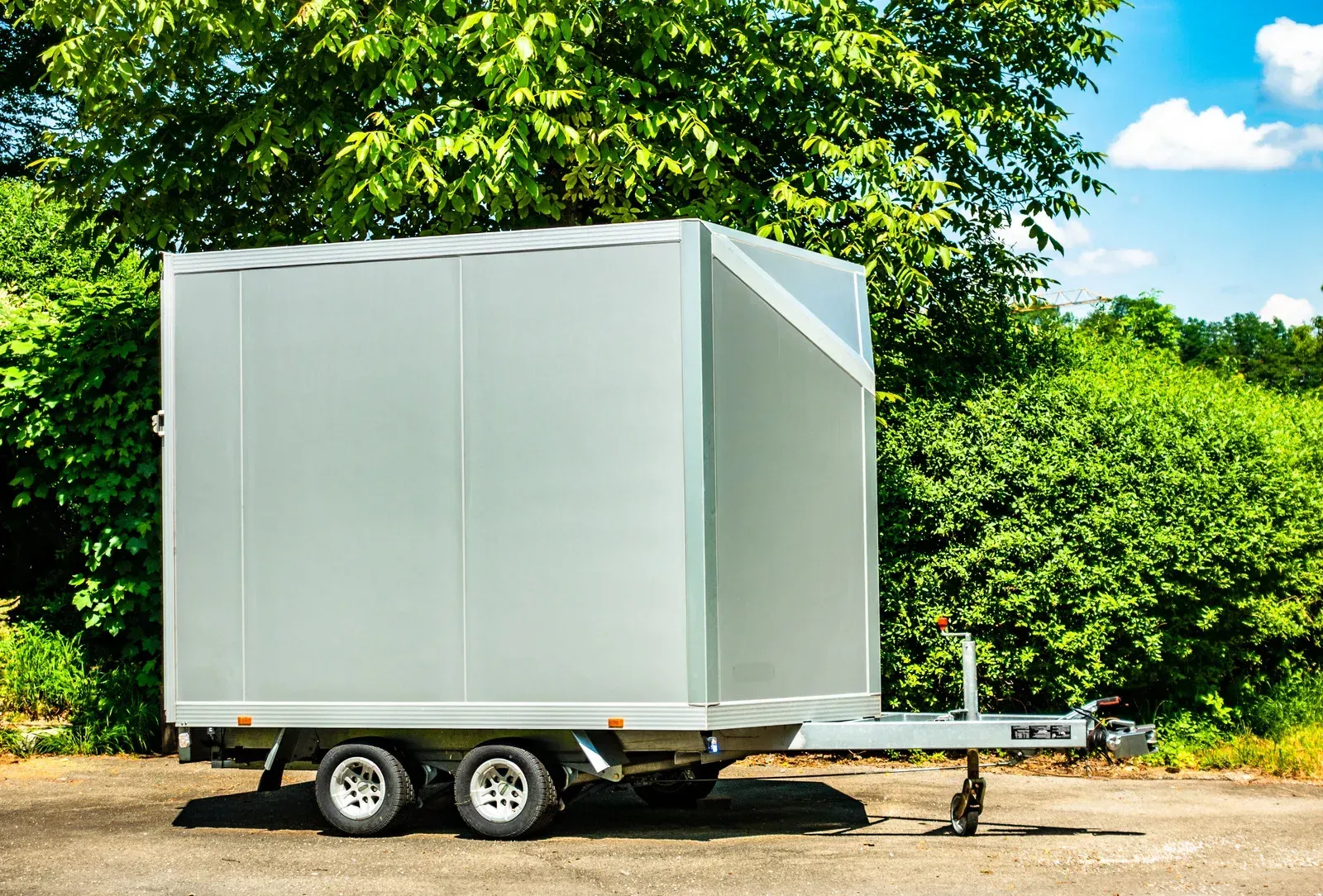 A white trailer is parked in a parking lot next to trees.