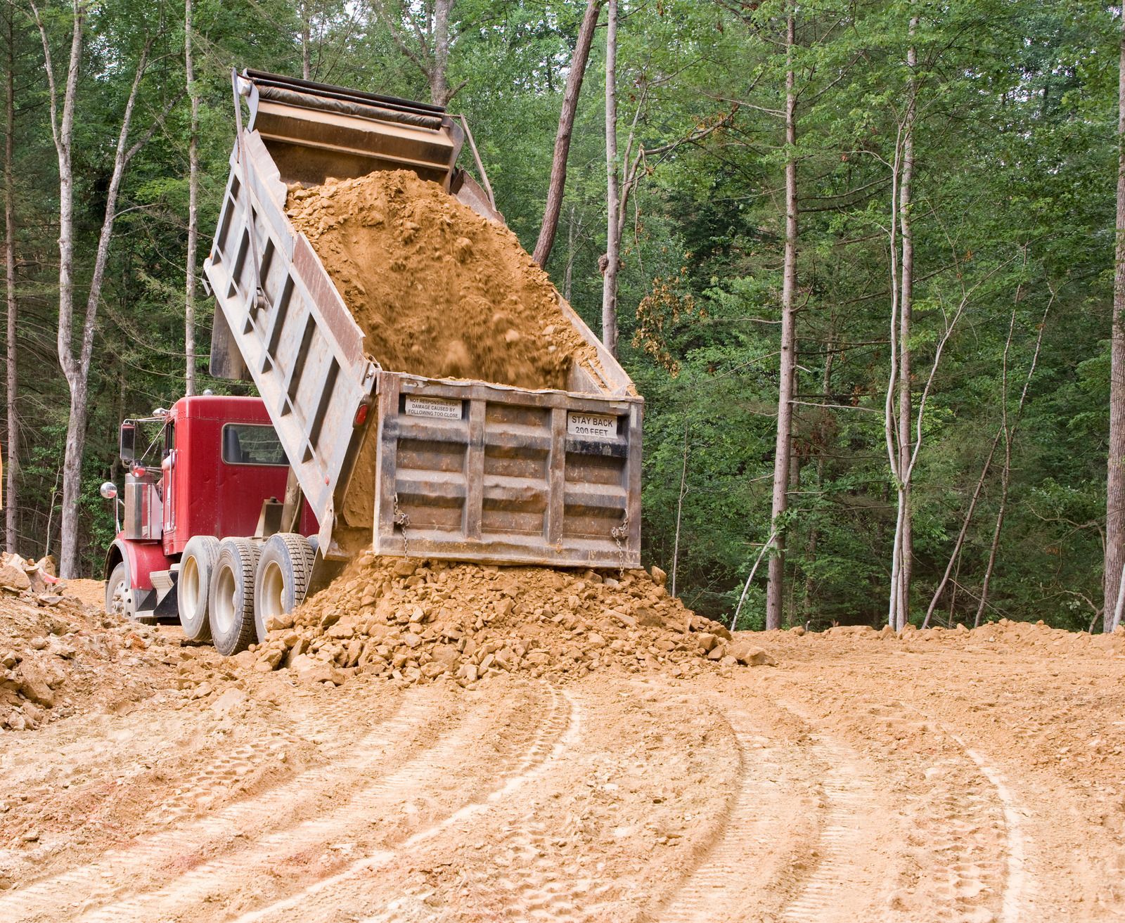A dump truck is dumping dirt on a dirt road