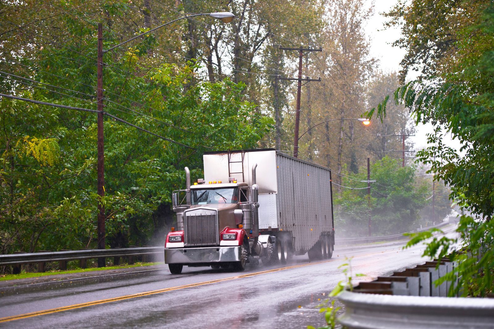 A semi truck is driving down a wet road in the rain.
