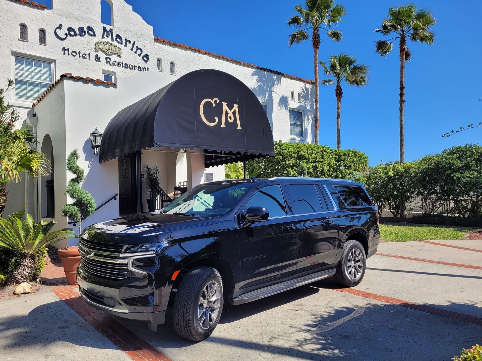 Black SUV parked outside Casa Marina Hotel under a navy CM awning, with palm trees and blue sky.
