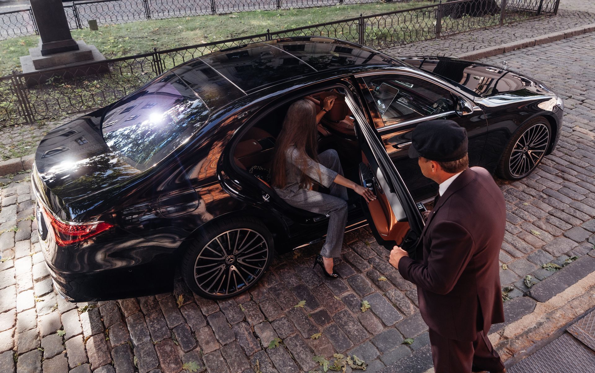 Man helping a woman out of a black car on a cobblestone street at night