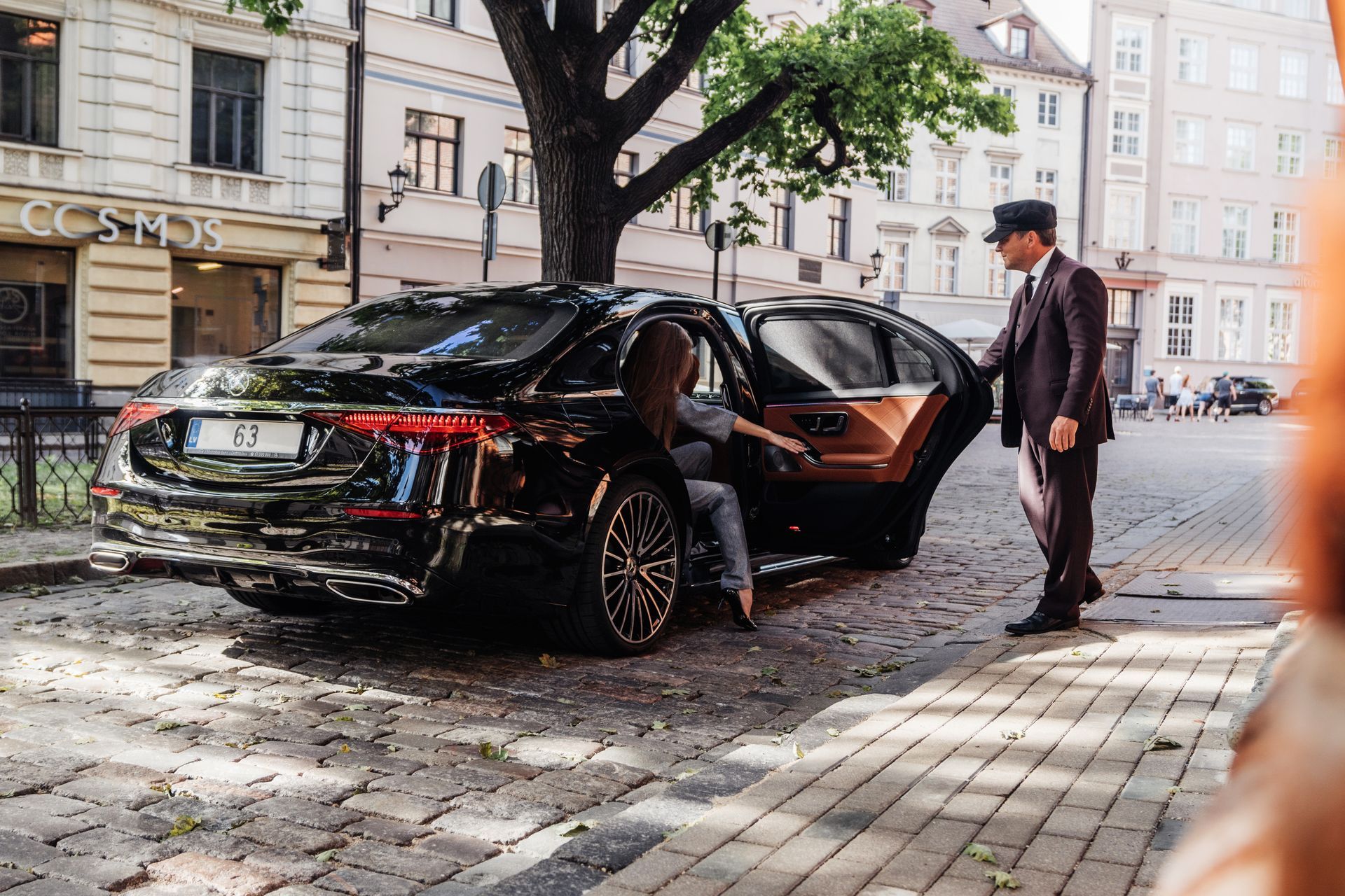 Black sedan with open door on a cobblestone street, with a man standing beside it in a city setting