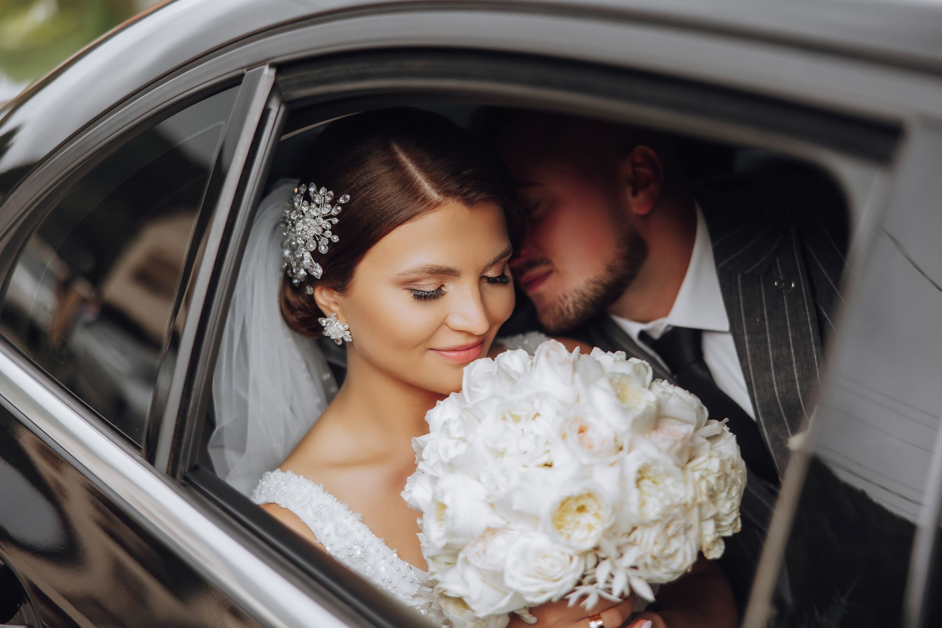 Bride and groom kissing in a car, bride holding a white bouquet