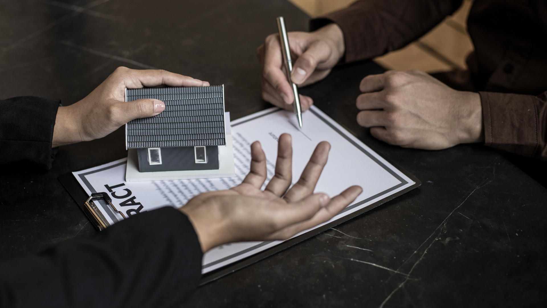 A person is holding a model house and signing a contract.
