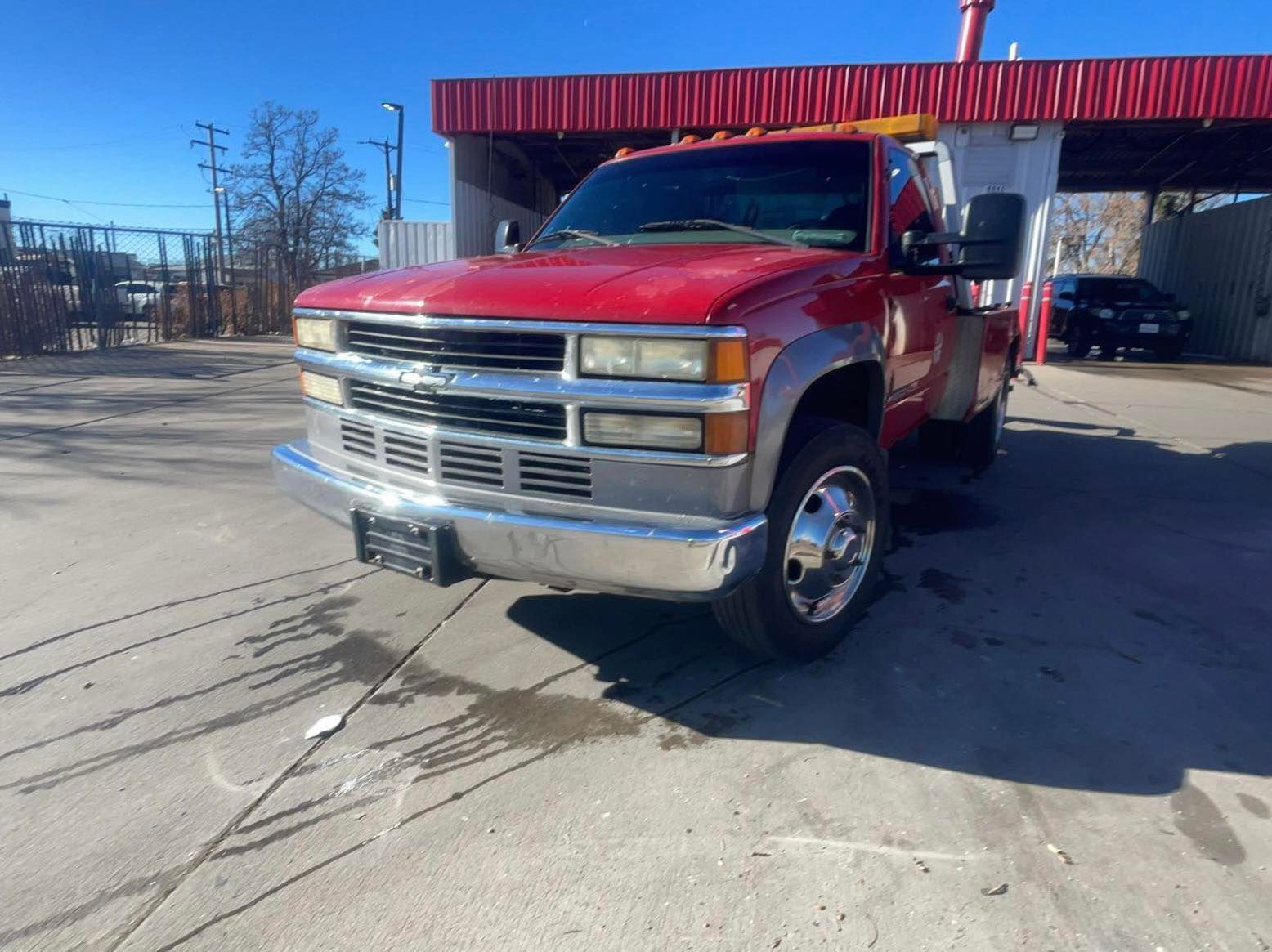 Red Chevrolet tow truck parked in front of a red building on a sunny day.