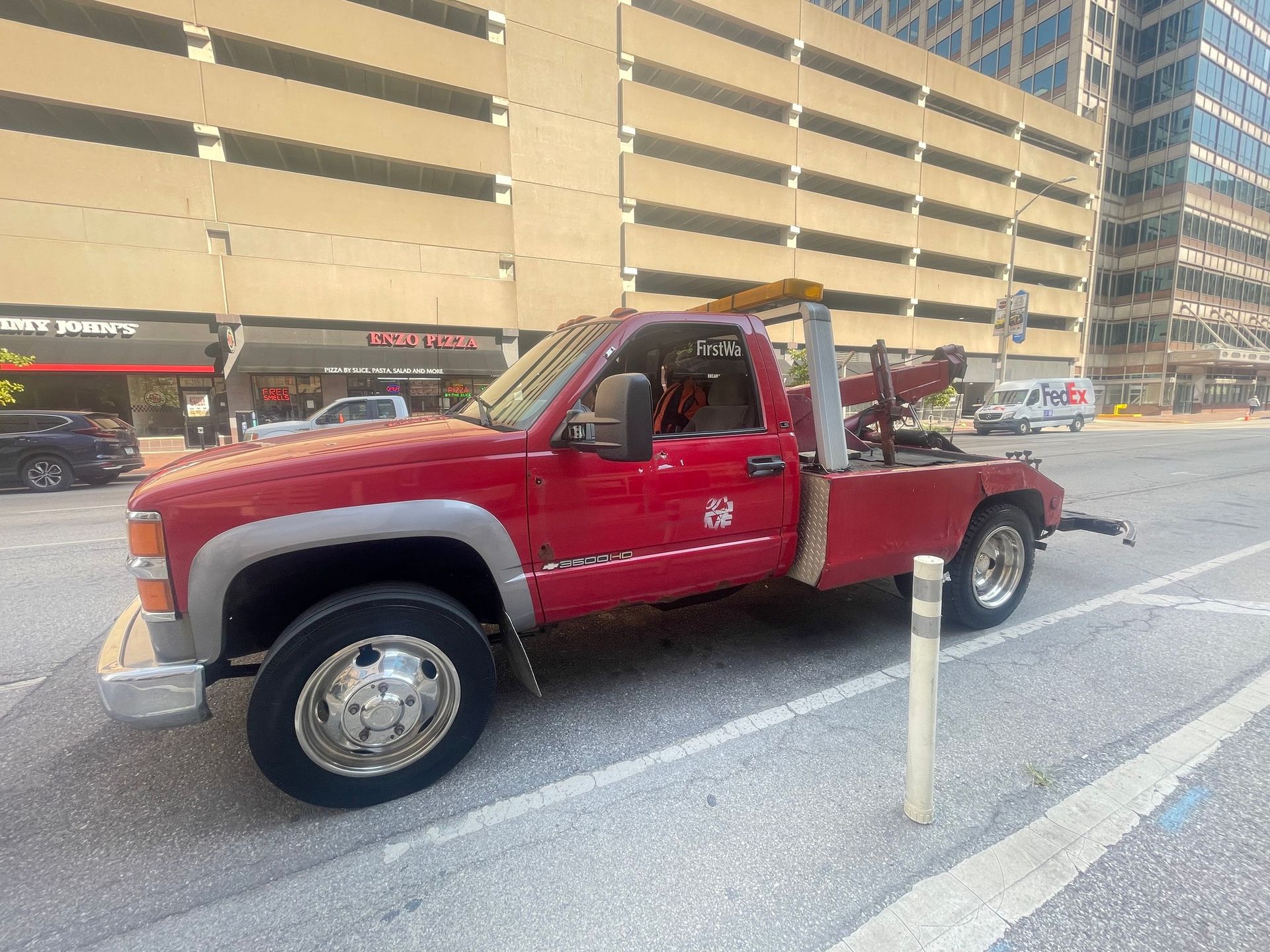 Red tow truck parked on a city street in front of a parking garage.