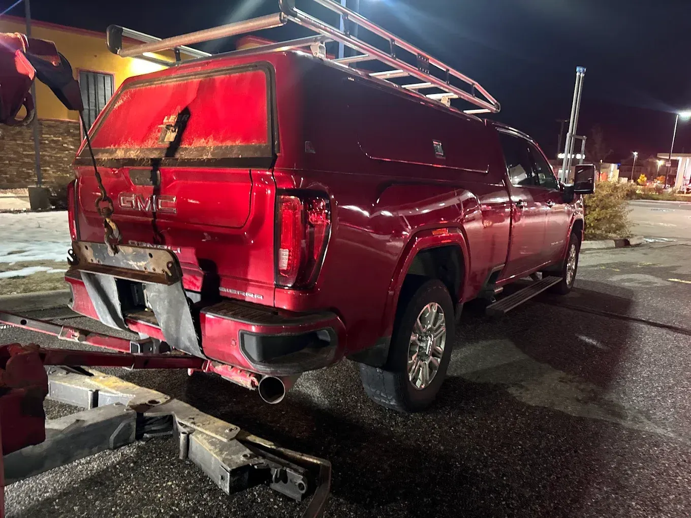 Red truck with damaged rear being towed at night.