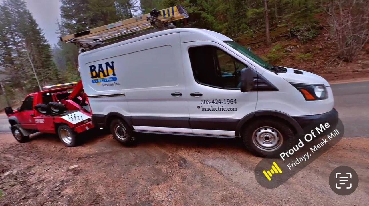 White service van towing a red car on a dirt road; van has 