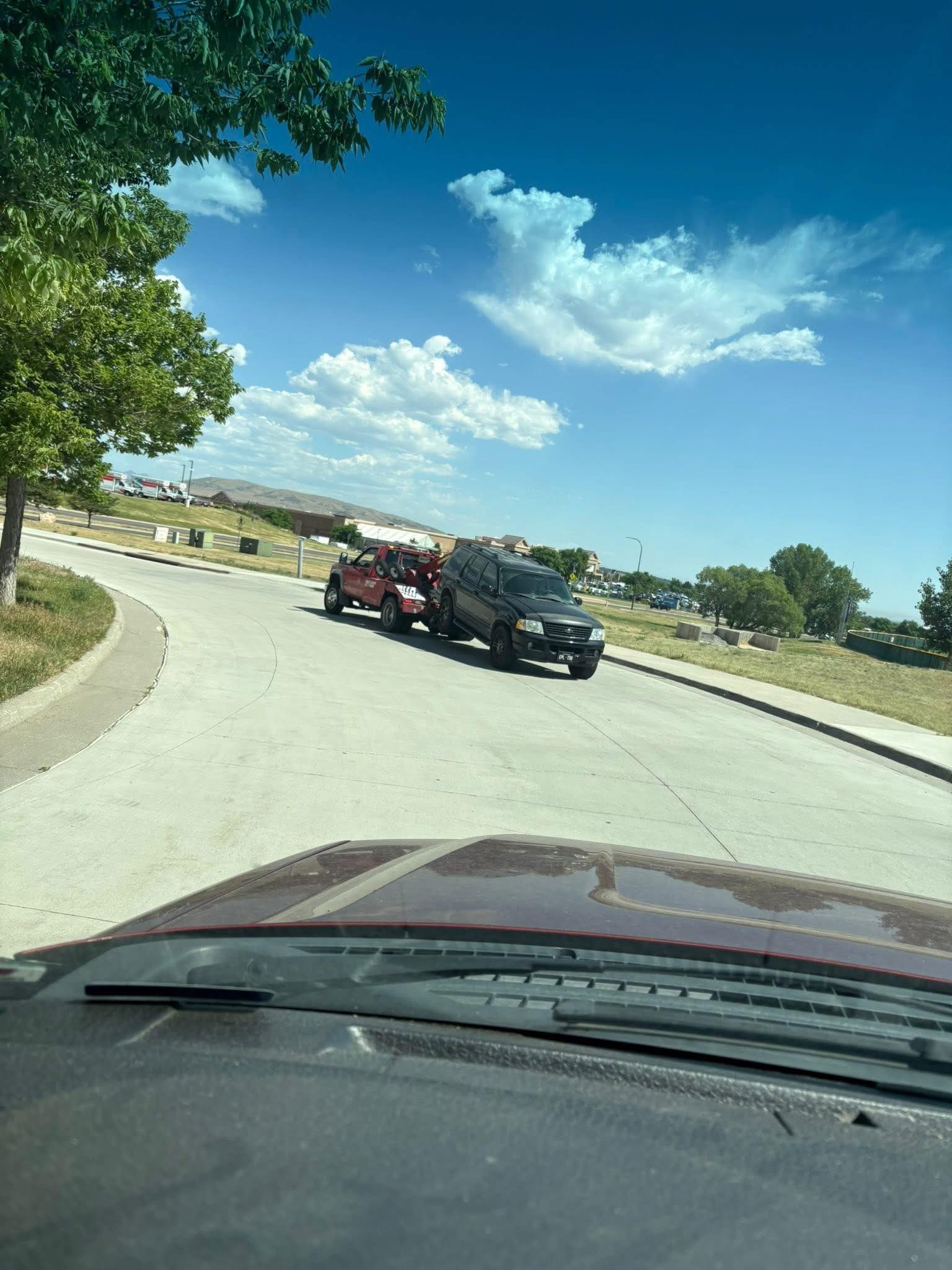 Two trucks on a curved road, one red, one black, under a blue sky with clouds.