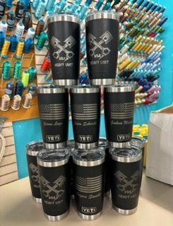 A stack of black Yeti tumblers with engraved designs: crossed pistons, US flag, and names.