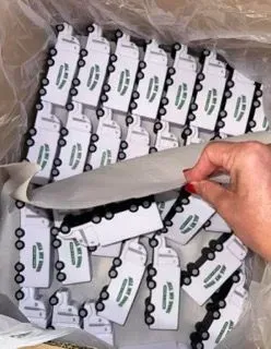 Box of white keychains with black accents and green logos; a hand reaches into the box.